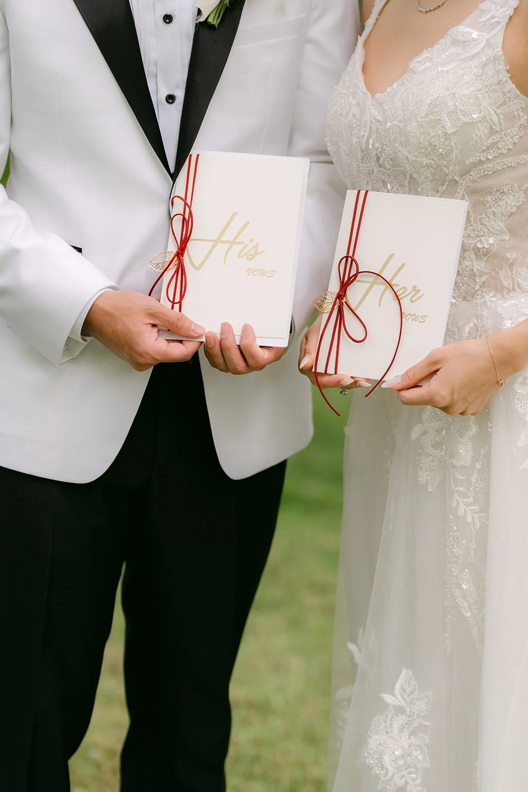 Jenny and Ryan holding white vow books tied with red ribbon.