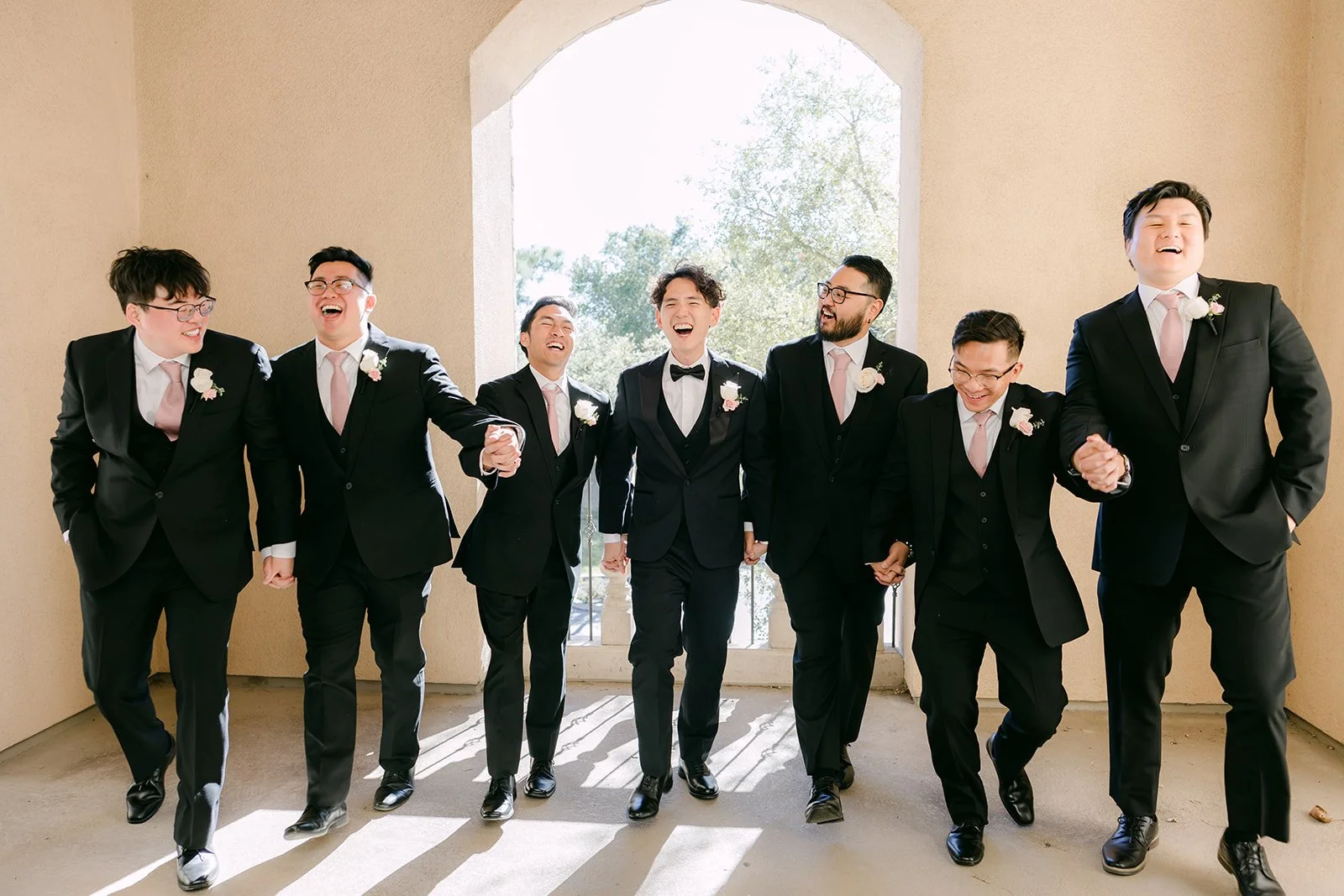 Groom and groomsmen laughing as they walk down an arched hallway