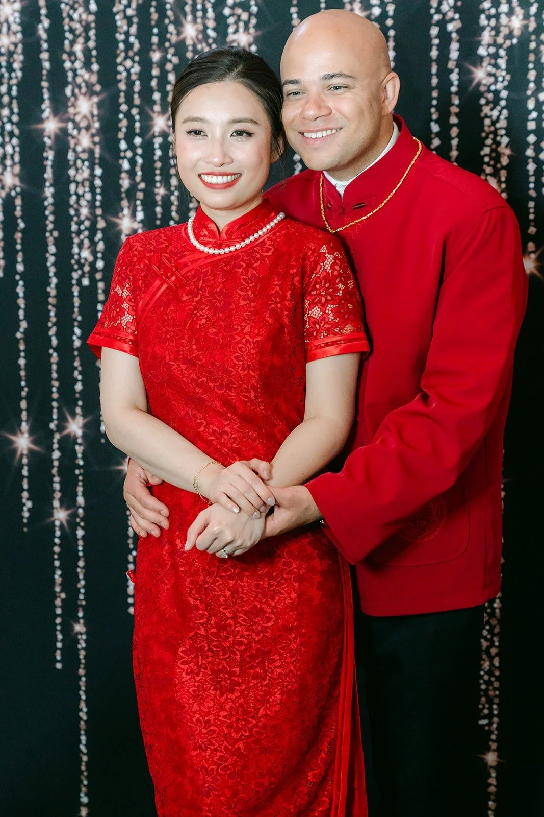 Elisa and Brandon in red in front of a sparkling backdrop, photographed by One and Only Production