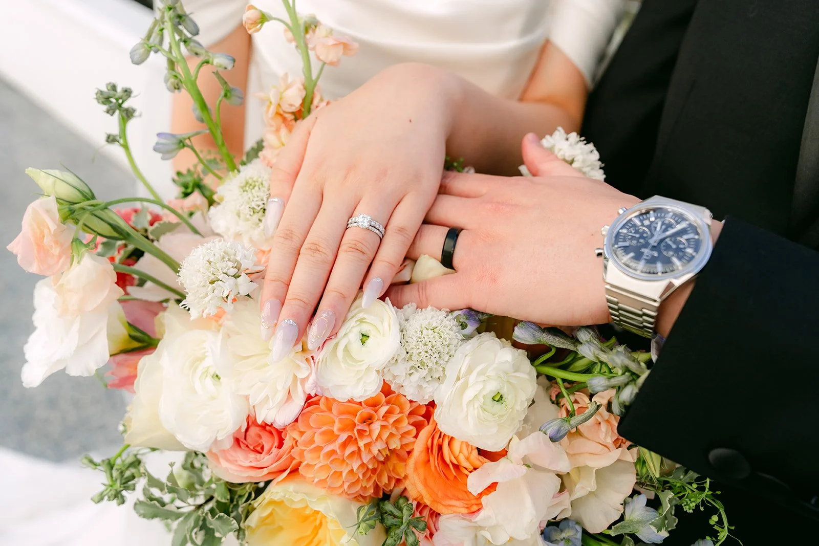 Amanda and San's hands and wedding rings over her bouquet.
