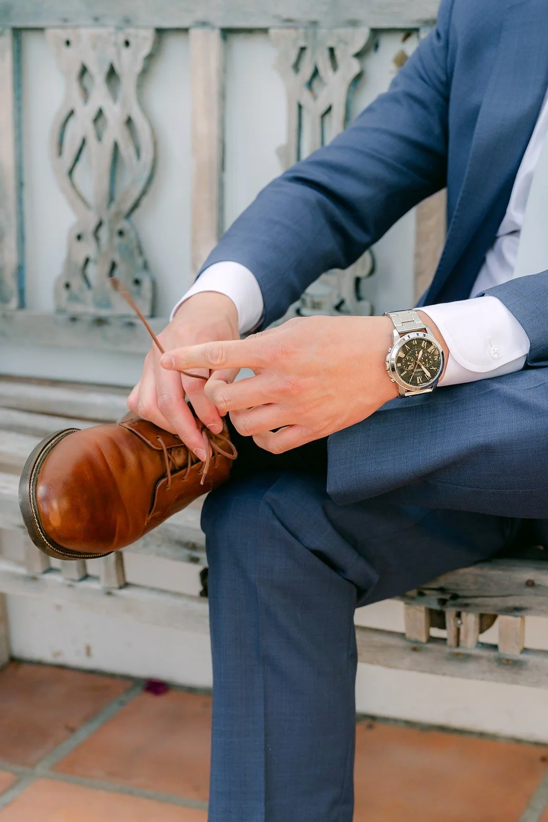 Jerrick tying his brown dress shoes on a carved bench