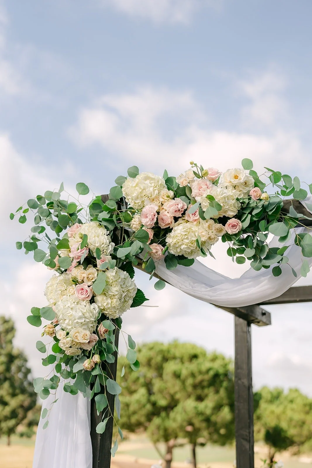Blush and ivory florals on the ceremony arch with the golf course behind