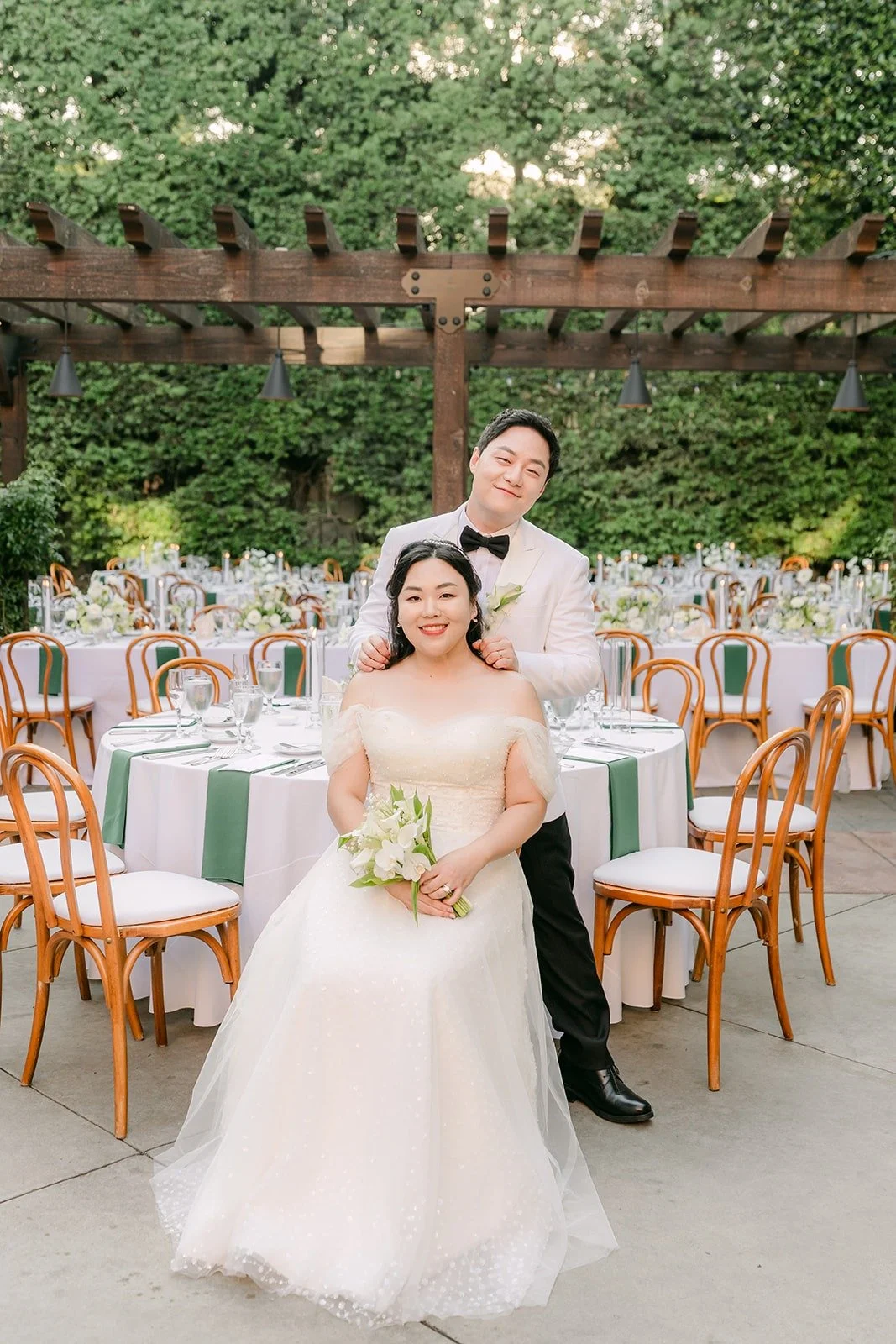 Chorok sitting with her bouquet while Min Soo stands behind her under the pergola