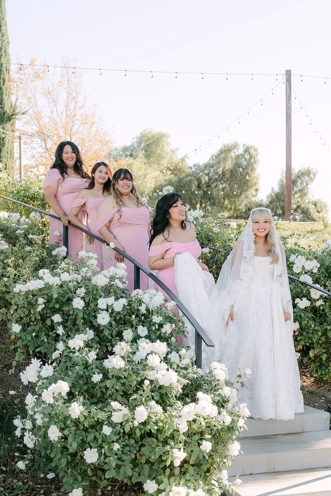 Konitha and her bridesmaids on the steps beside white roses