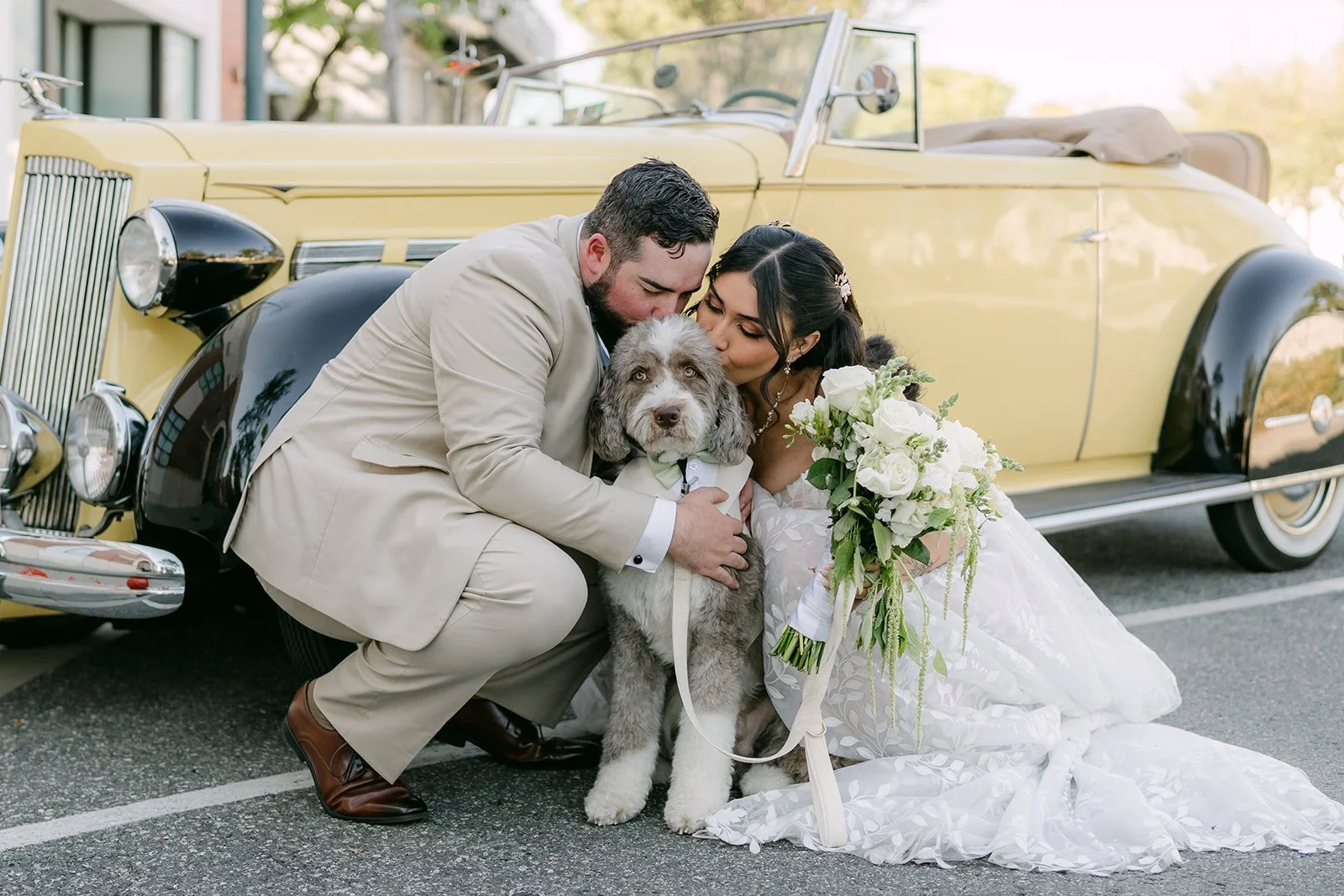 Fernanda and Cody posing with Olive beside a yellow vintage car.