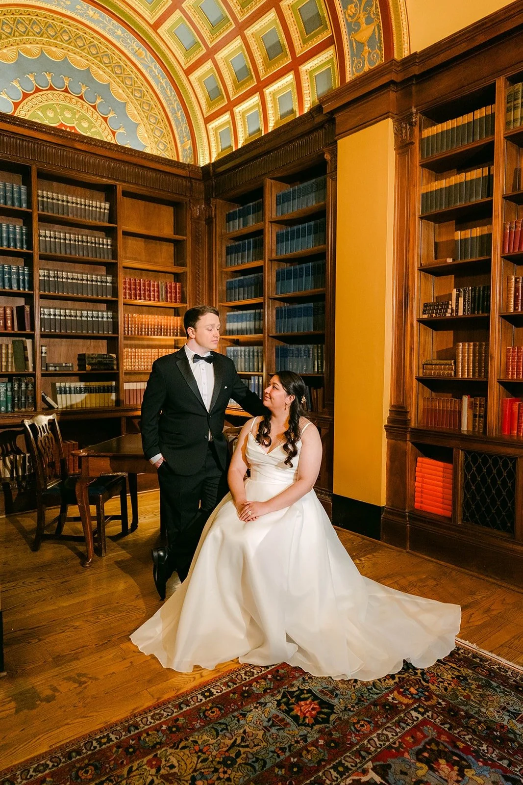 Saira and Matthew among the tall bookshelves of the library, photographed by One and Only Production
