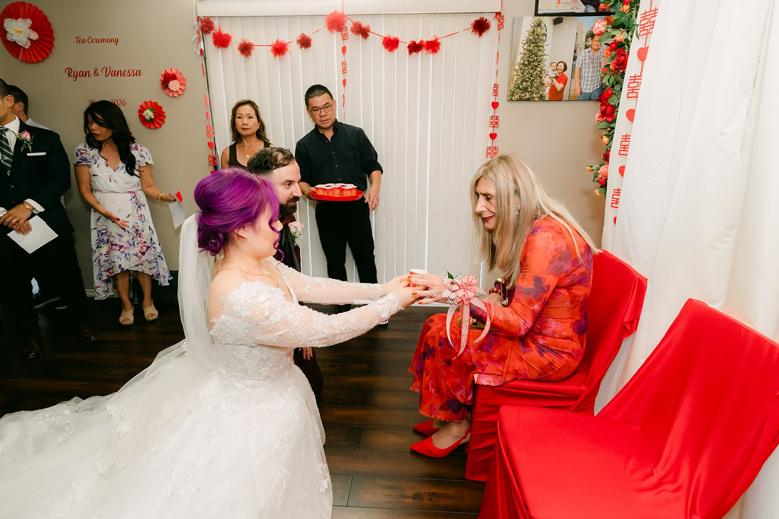 Vanessa kneeling to serve tea to an aunt in red.