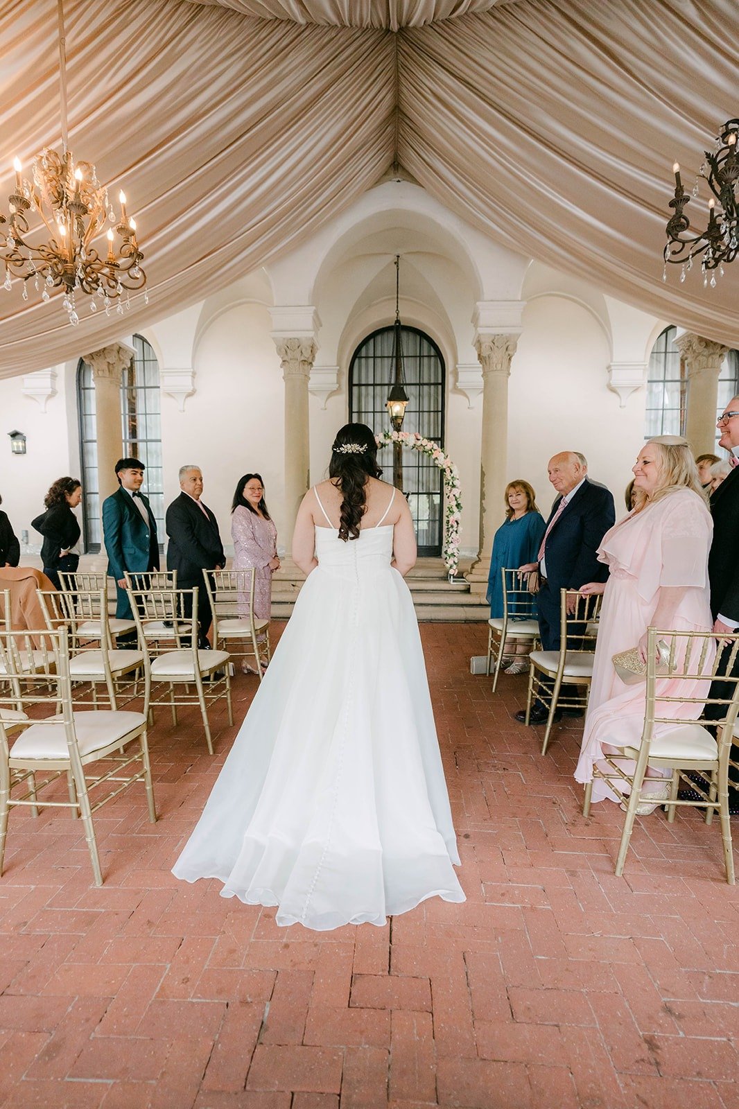 Saira walking down the aisle toward the rose arch as guests stand