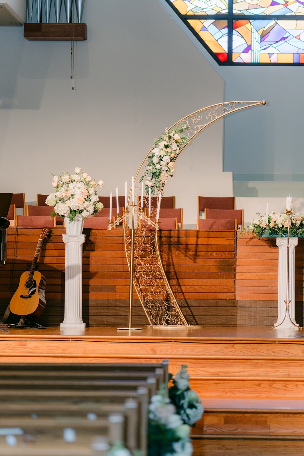 A gold arch with white florals set on the altar stage