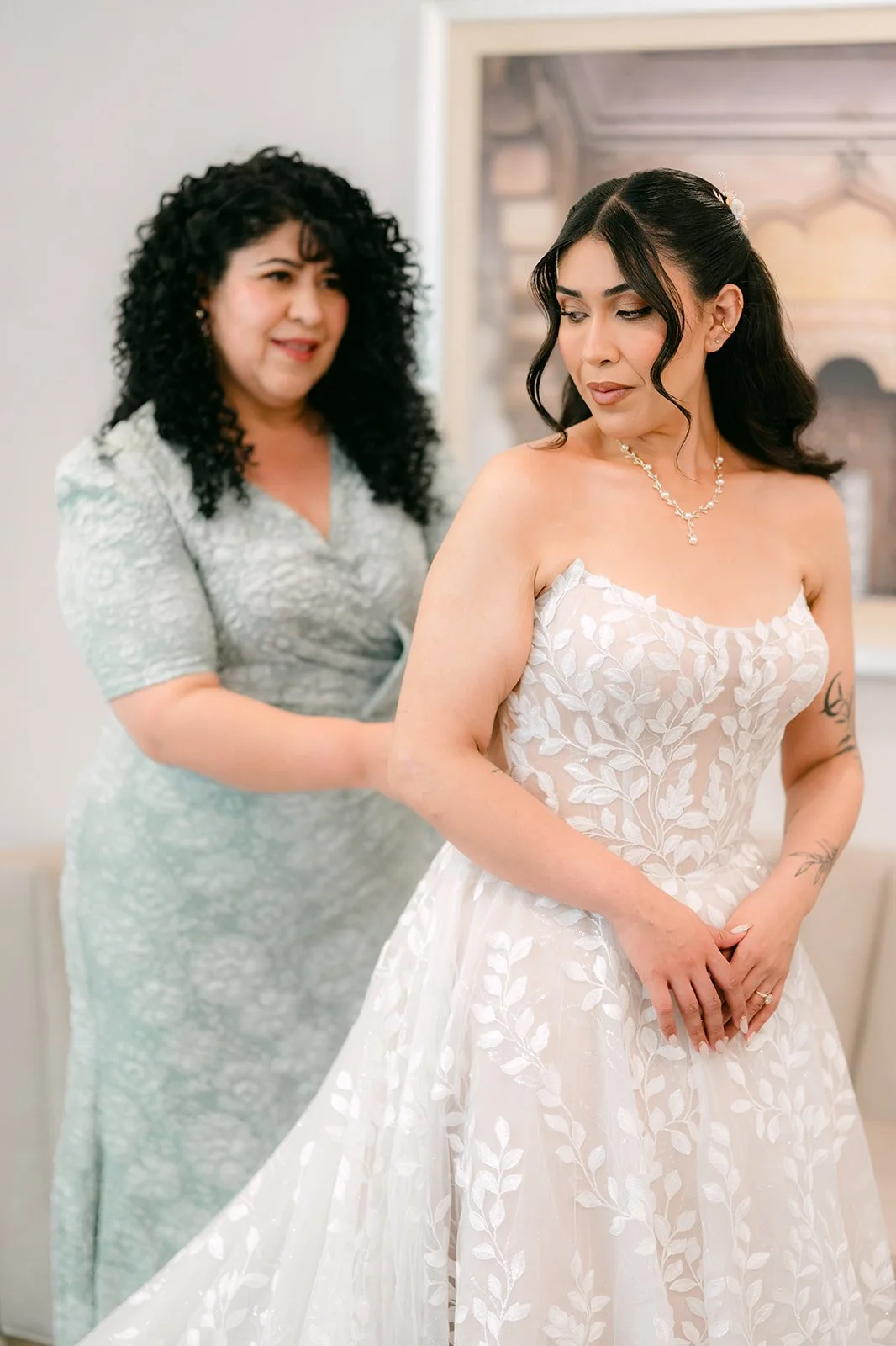 A bridesmaid in sage helping Fernanda into her gown.
