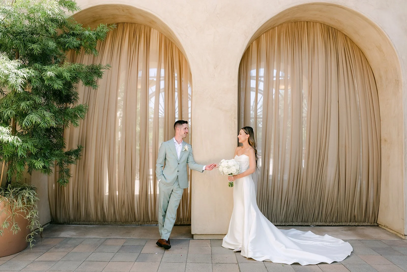 Kieu and Anthony between two arches and potted olive trees, photographed by One and Only Production