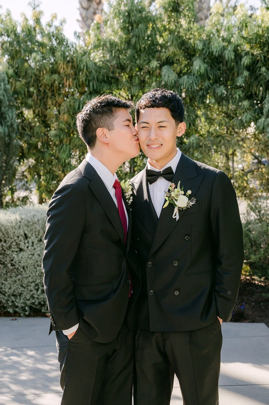A groomsman giving Richard a kiss on the cheek outside, photographed by One and Only Production