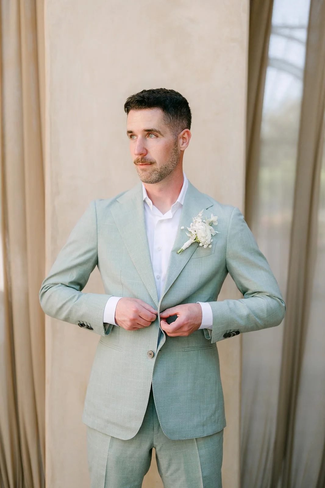 Anthony buttoning his sage green suit jacket