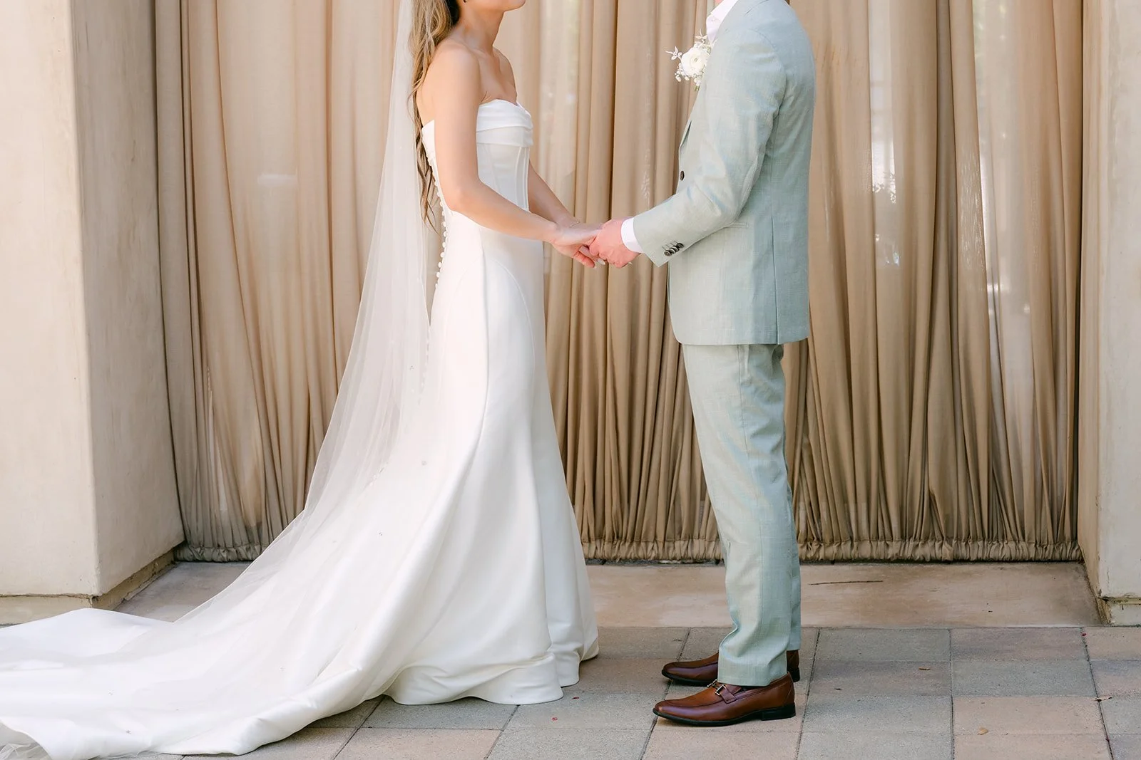 Couple holding hands during their first look in front of the drapery