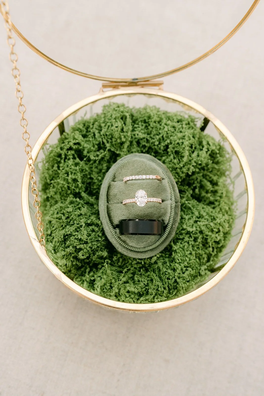 A green ring box nestled in moss inside a gold ring