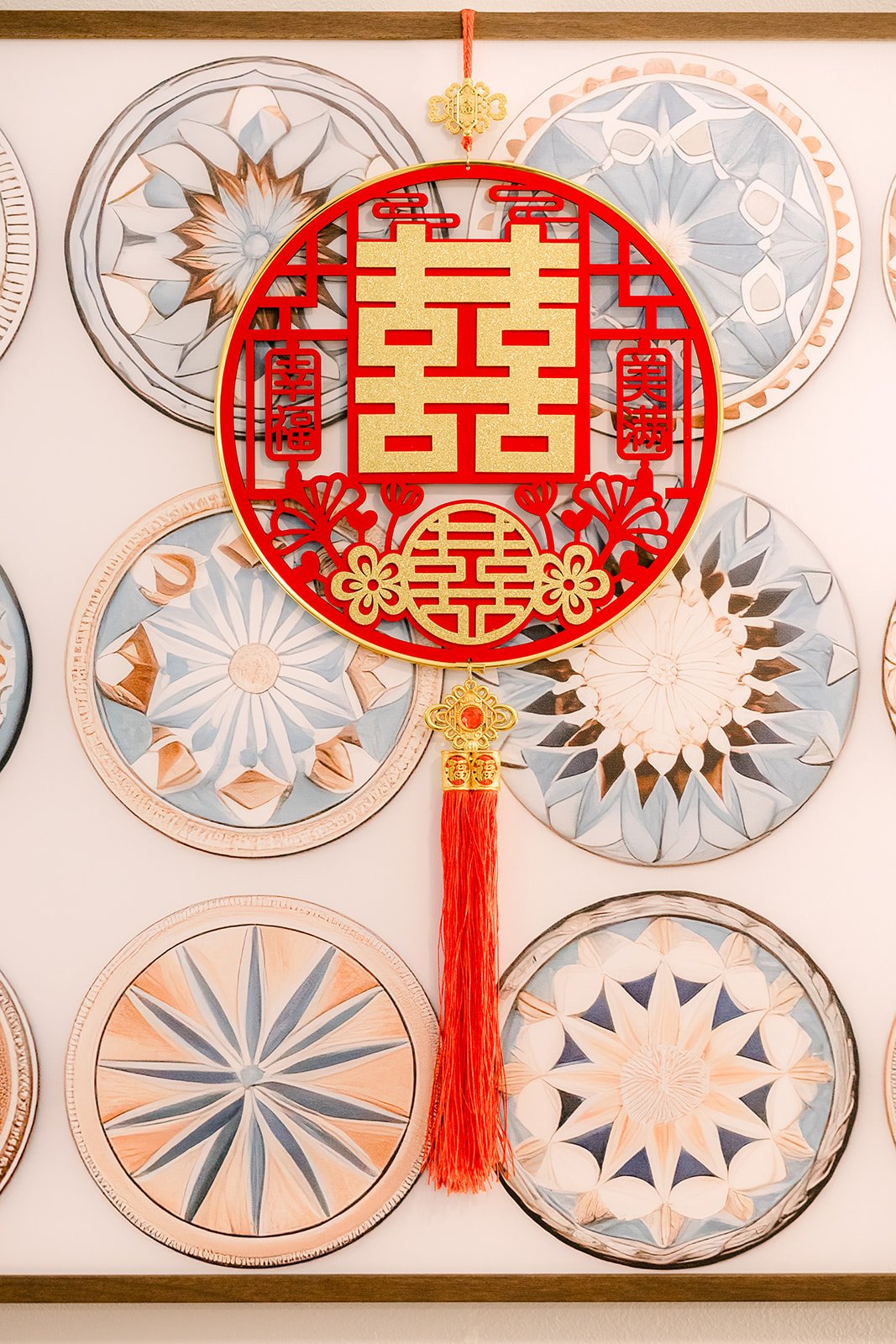 A red double happiness tassel ornament hung over a wall of decorative plates.