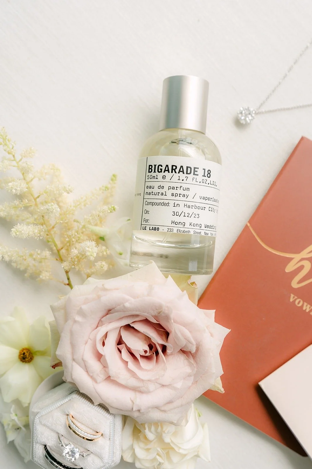 A perfume bottle with blush roses and a terracotta envelope in the flat lay