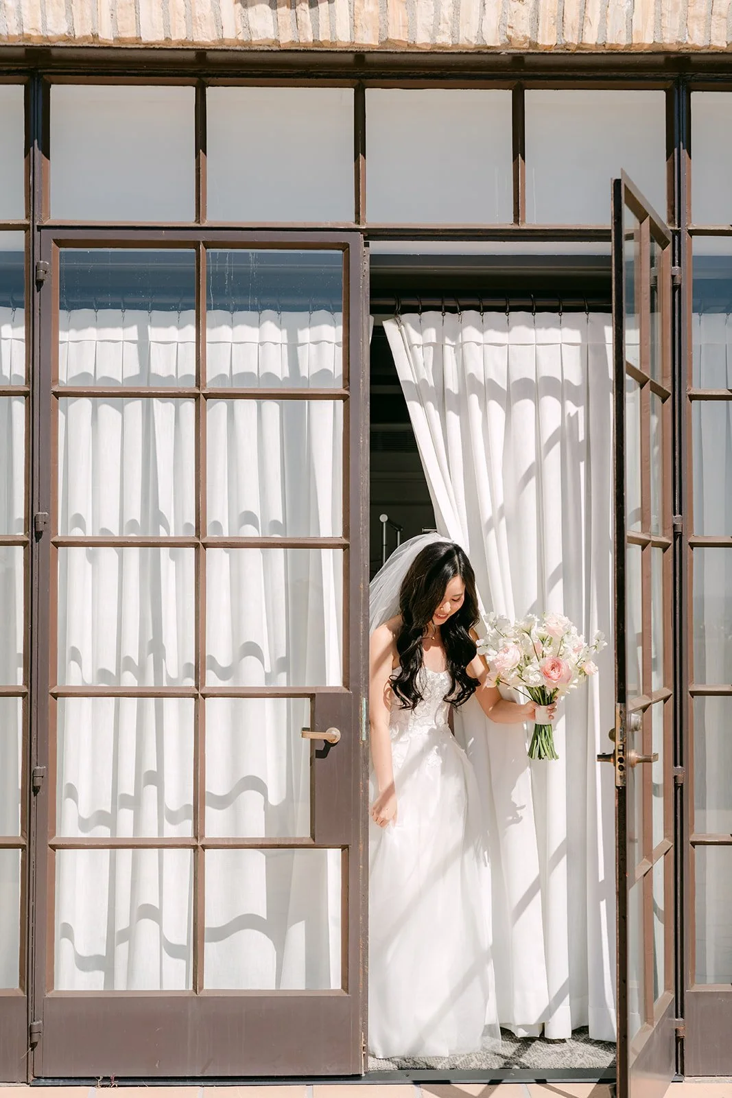 Bride stepping through French doors holding her bouquet