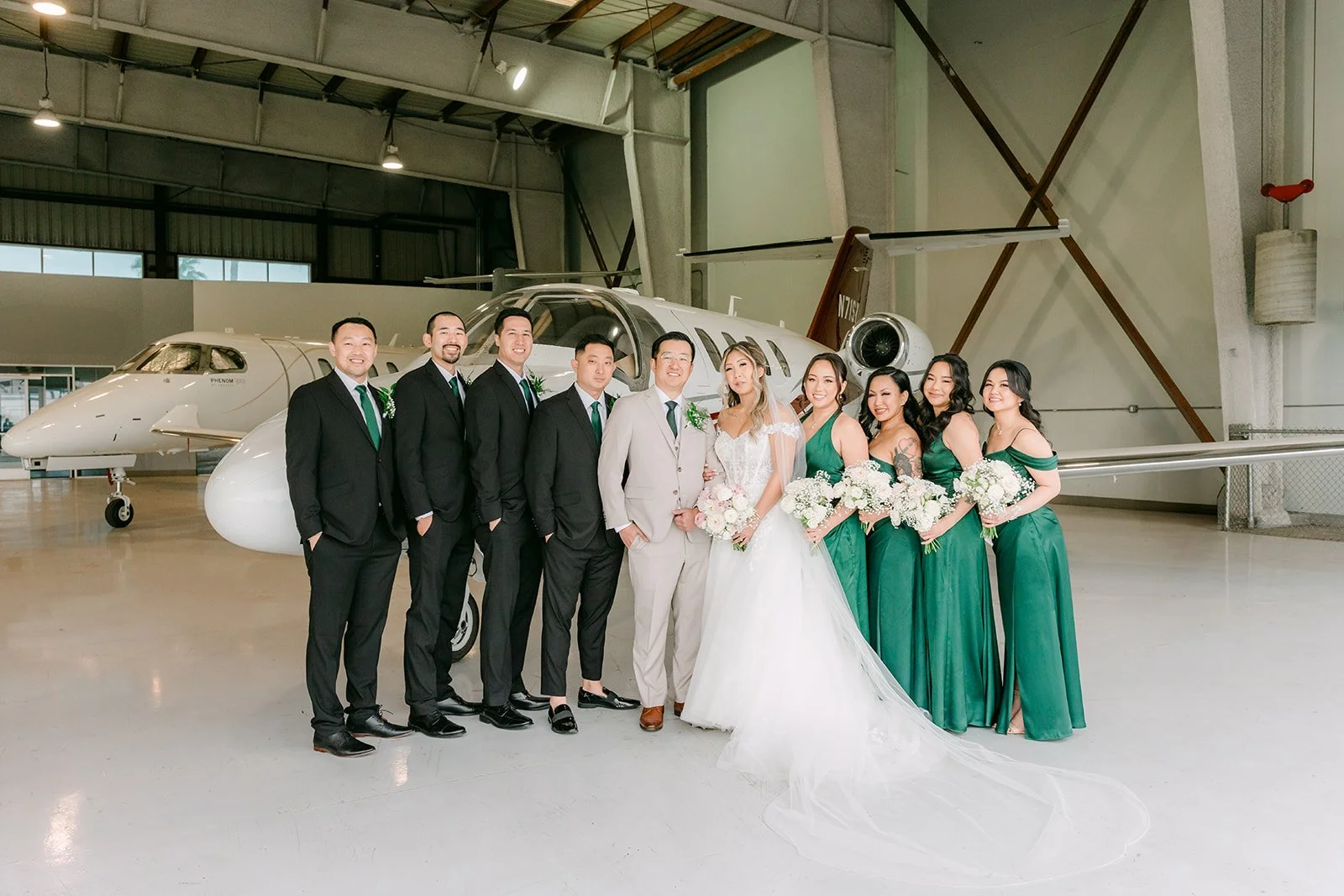 Full wedding party posing beside a private jet inside an airplane hangar