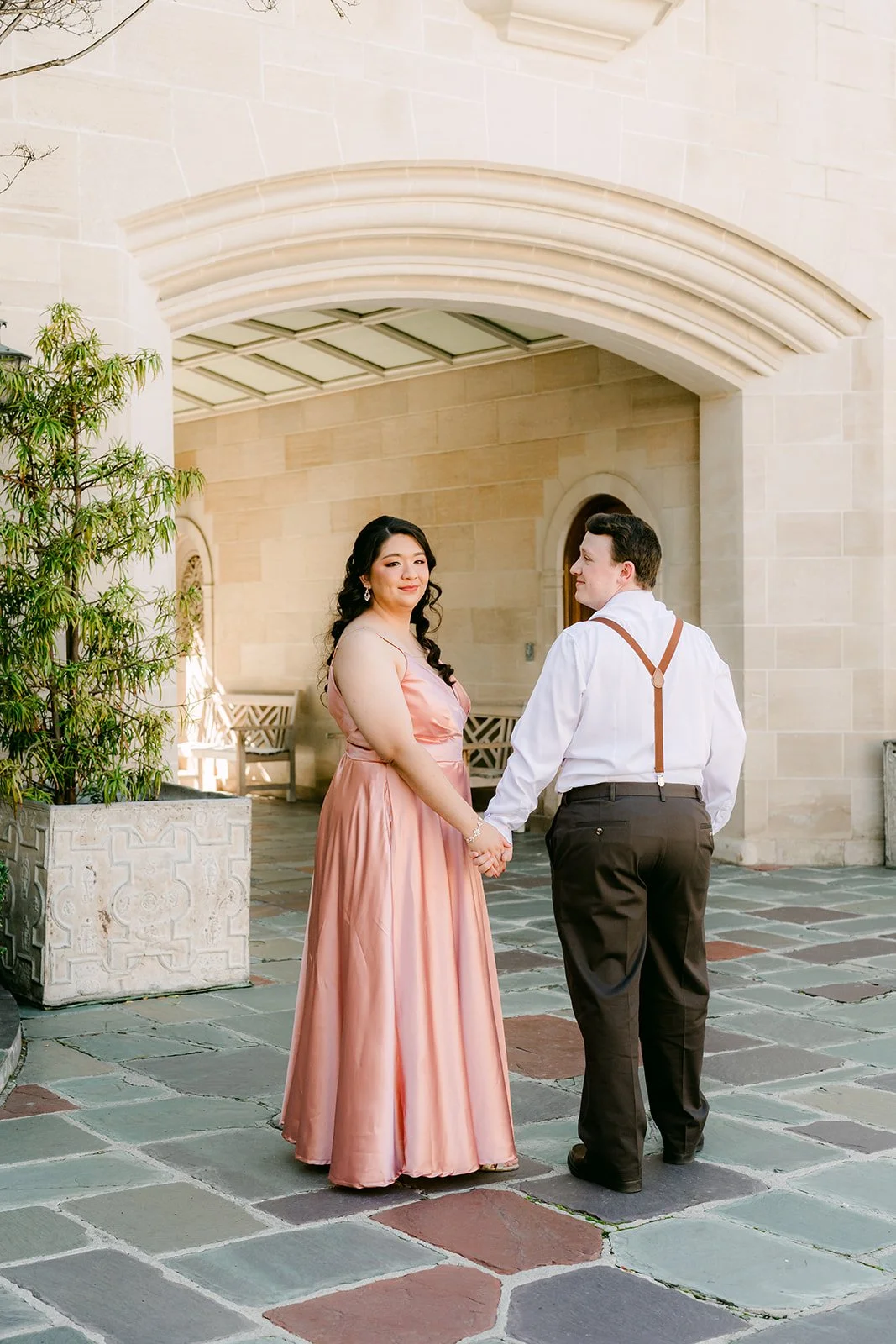 Saira and Matthew holding hands under the arched stone loggia.