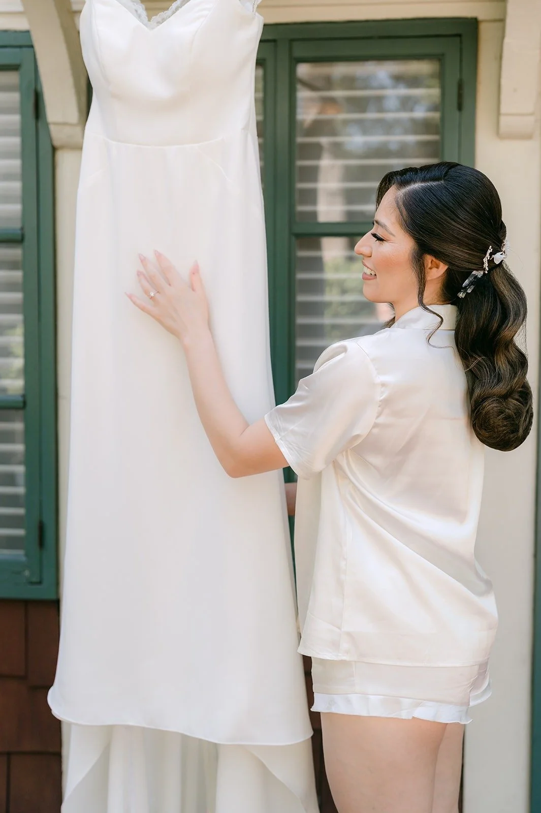 Mariana in a white satin robe reaching for her wedding gown