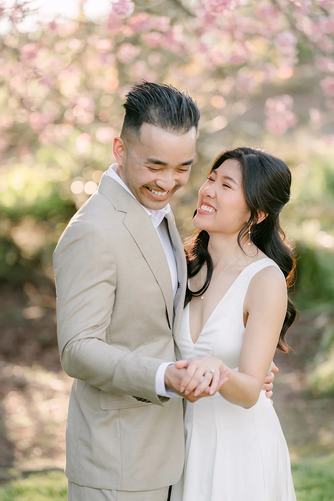 Kim and Vincent smiling together in front of soft pink blossoms.
