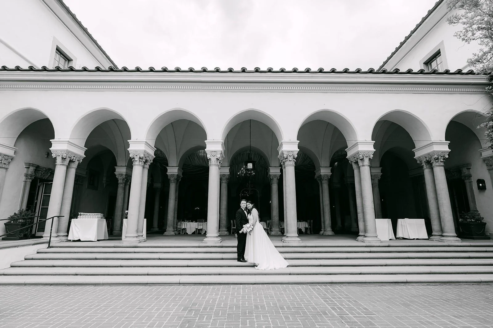 A black and white wide view of Saira and Matthew on the steps in front of the arcade