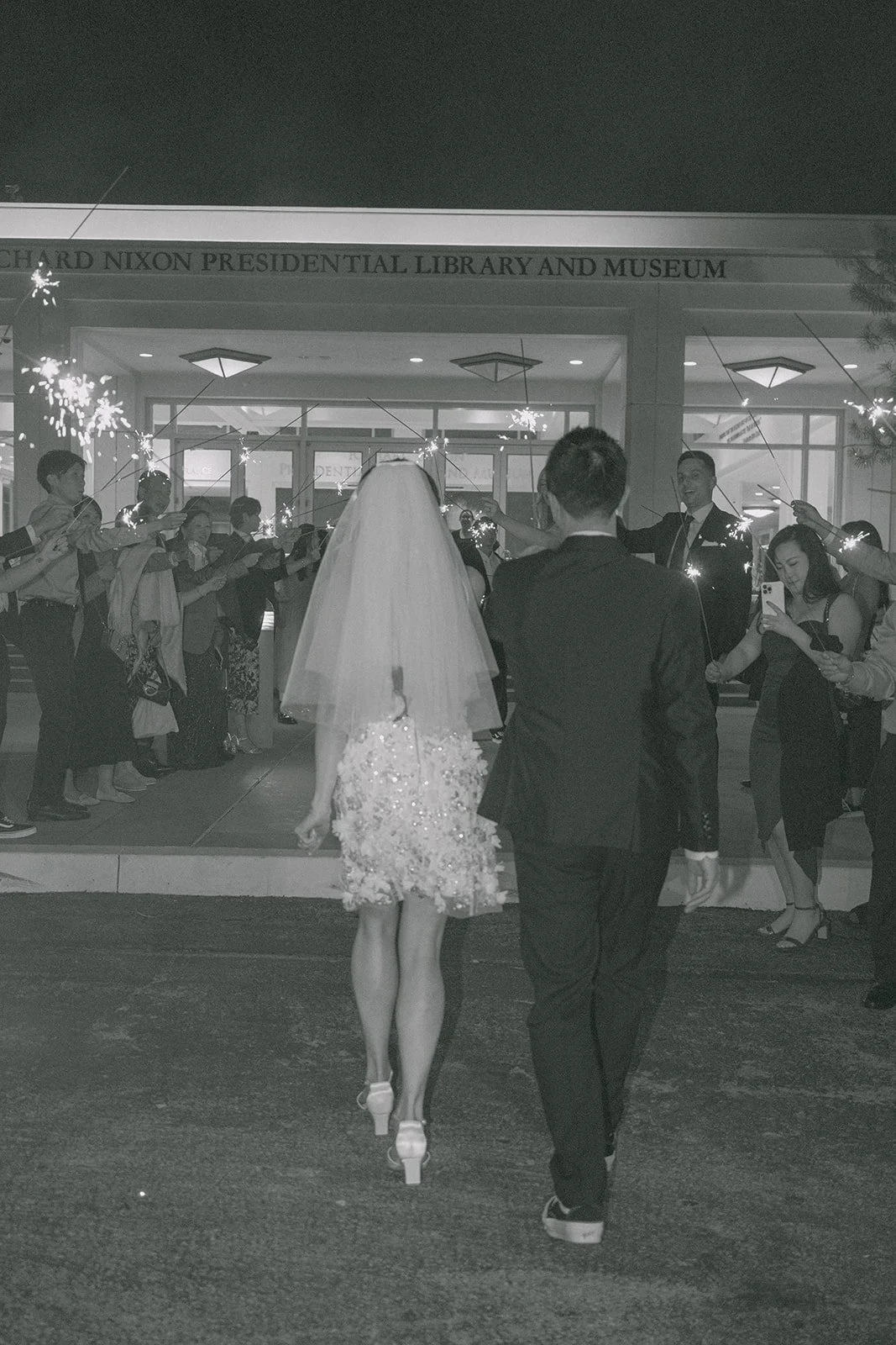 Black and white photo of Jenny and Ryan leaving through their guests, photographed by One and Only Production.