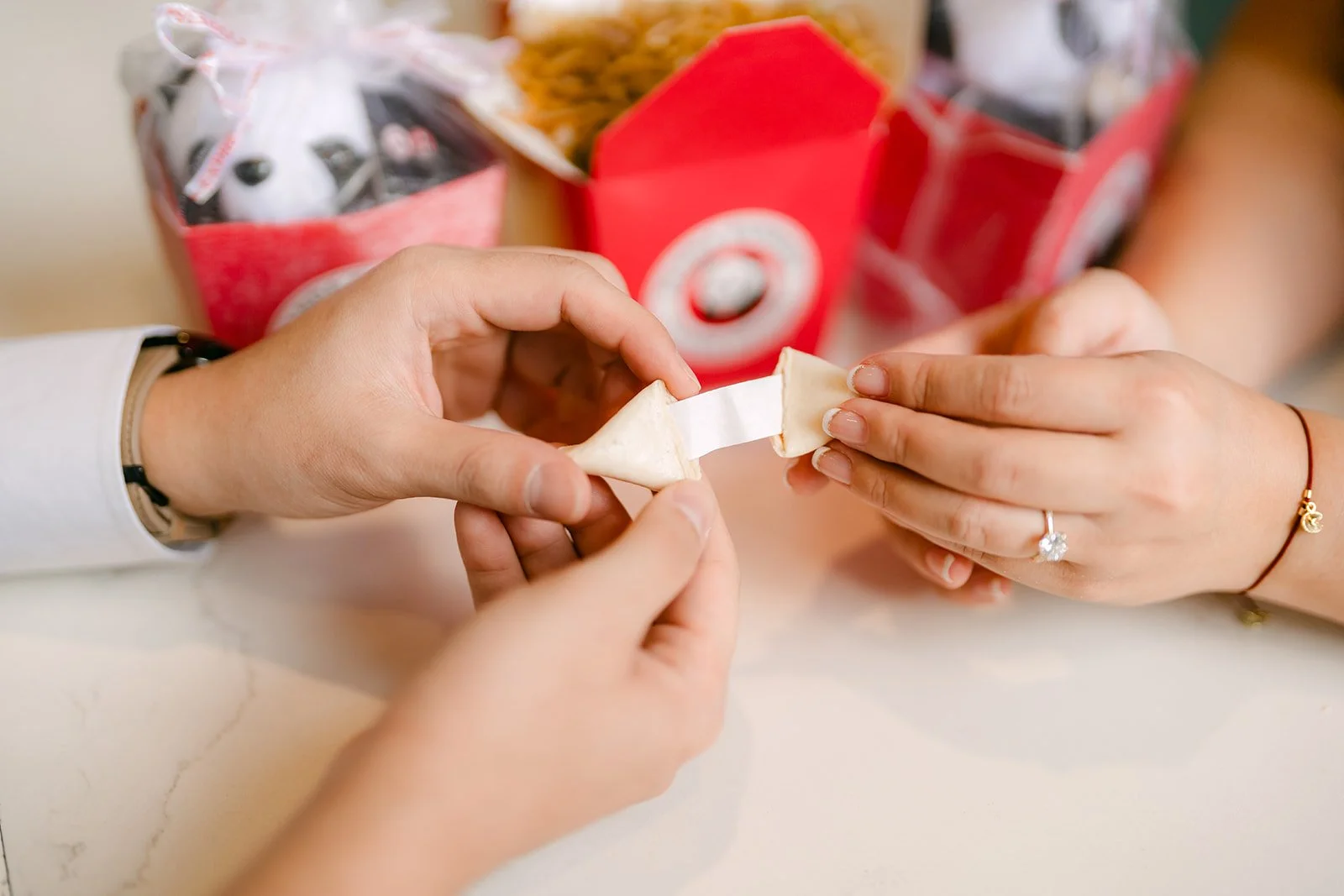 Linh and Ankush open fortune cookies together, her ring showing.
