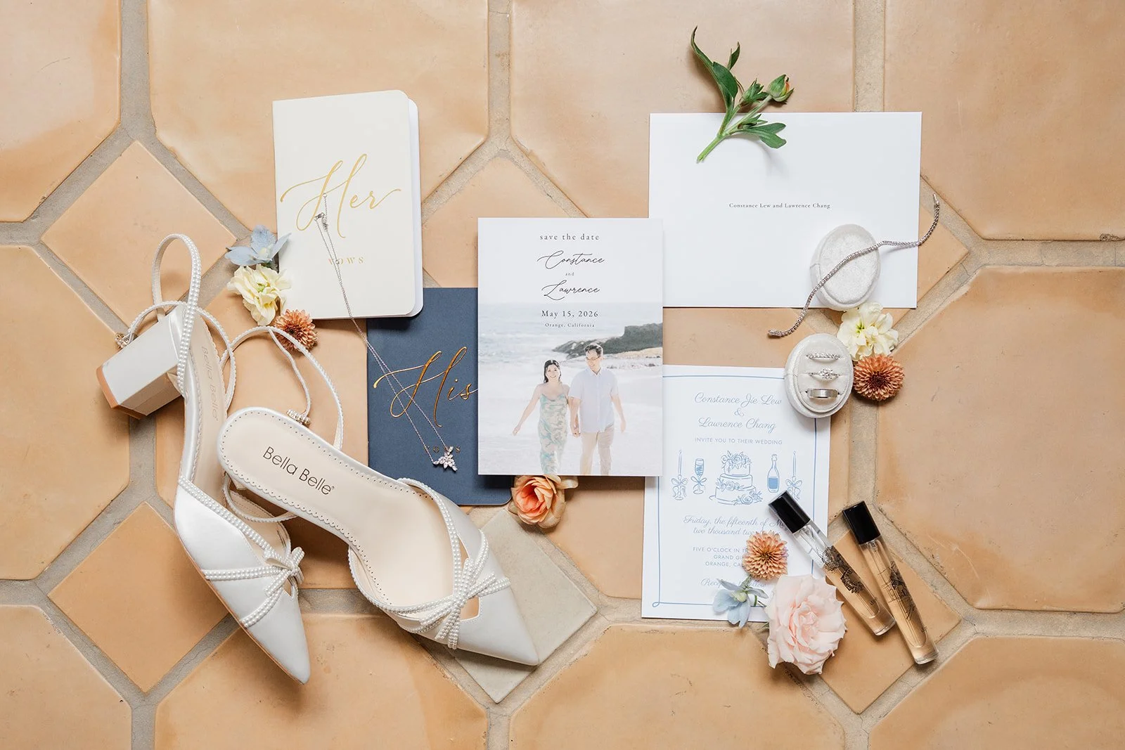 Wedding flat lay with a navy and white invitation suite, bridal heels and perfume on terracotta tile