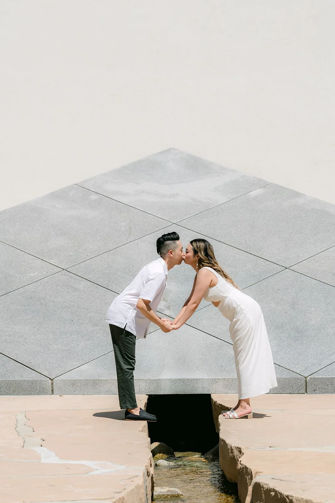Stephanie and Alan kiss over the stream in front of the pyramid.