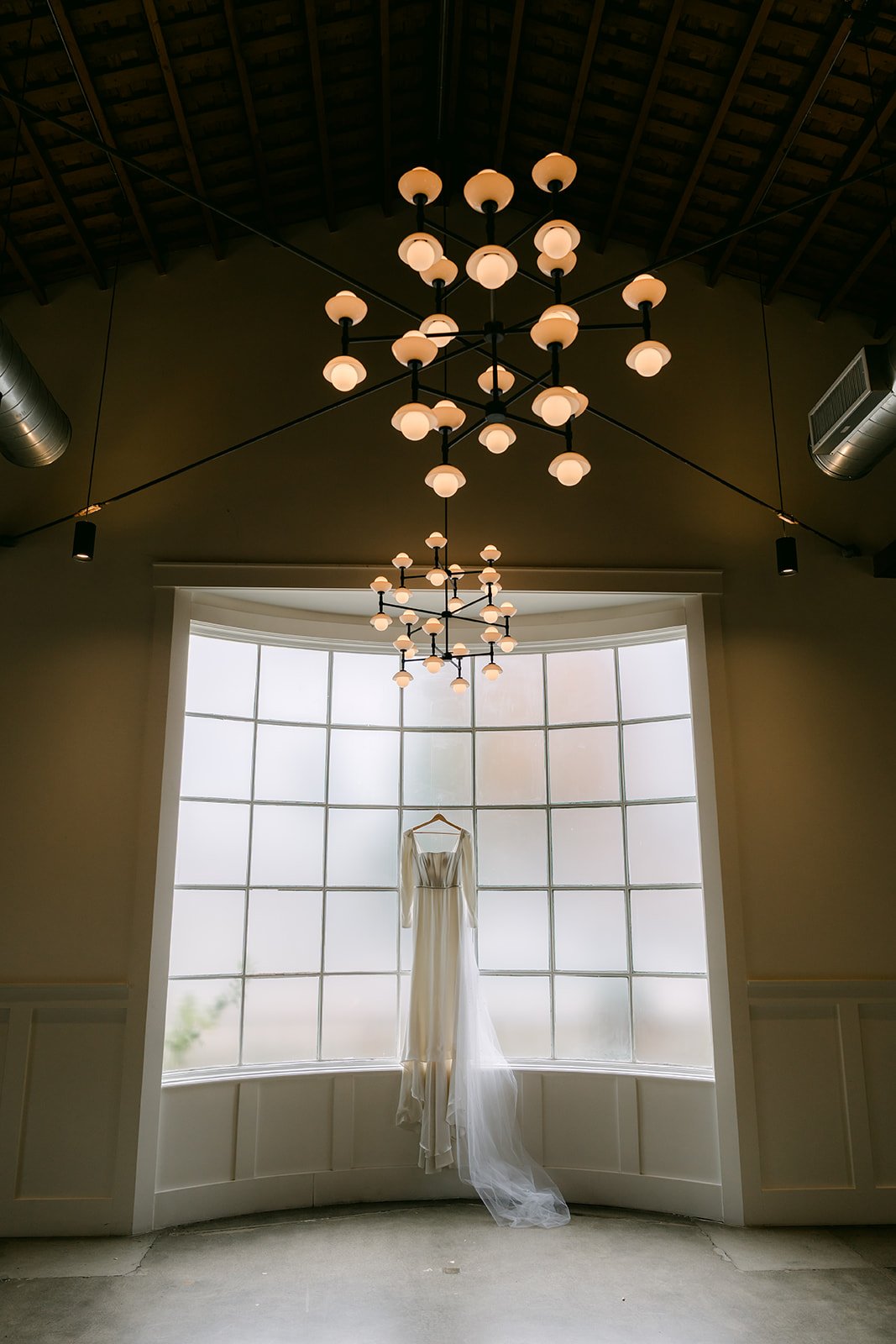 Denise's long-sleeve wedding gown hanging alone in the arched window.