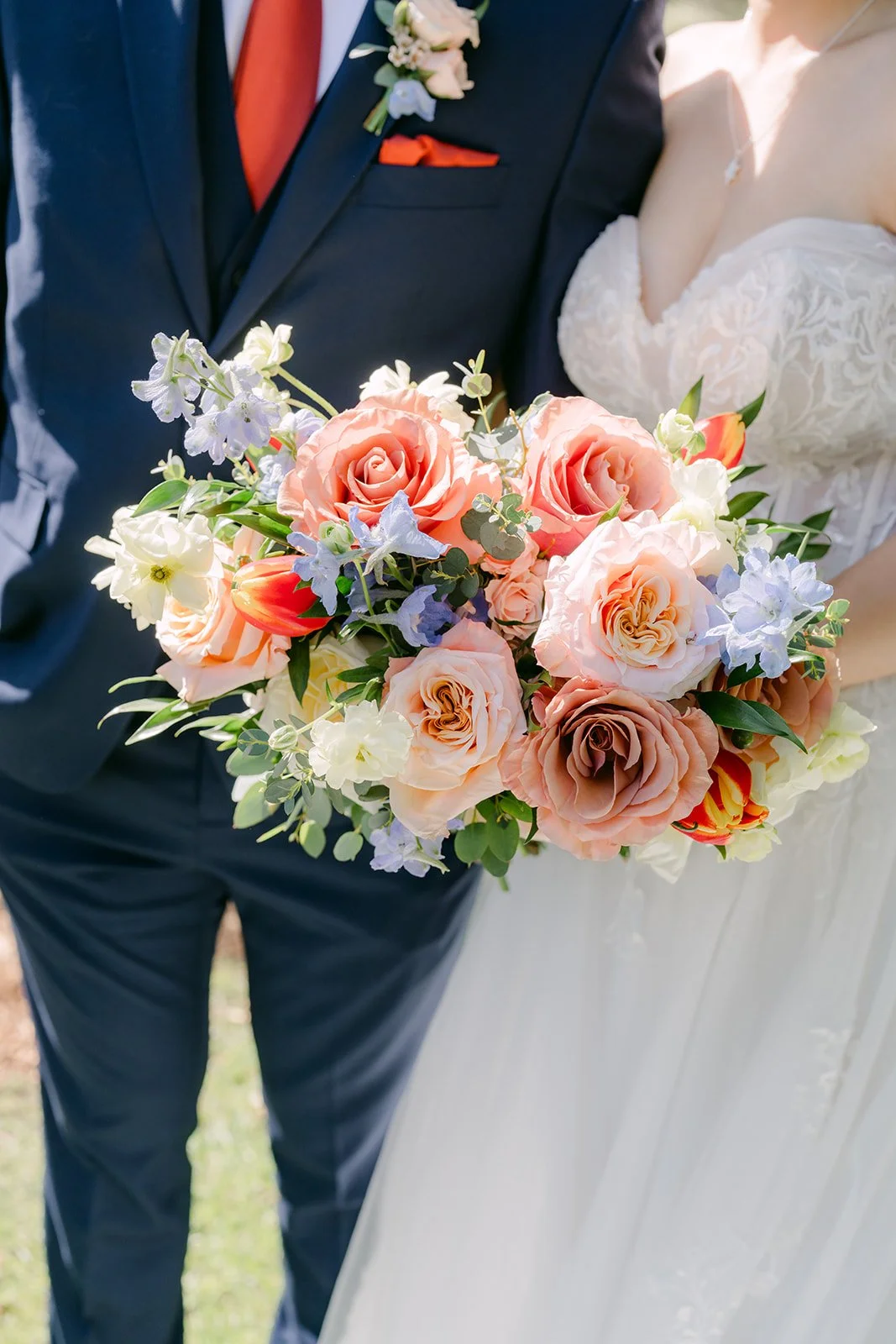 Close-up of the peach and blue bouquet held between the couple