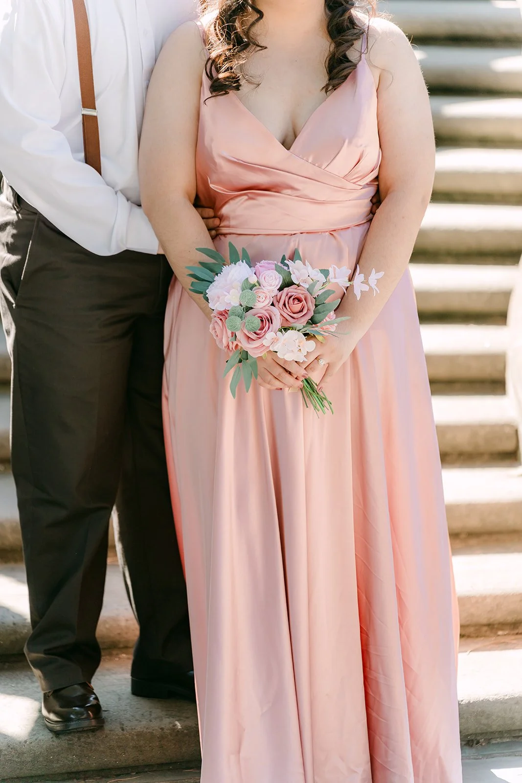 Saira holding a pink rose bouquet beside Matthew on the stone steps.