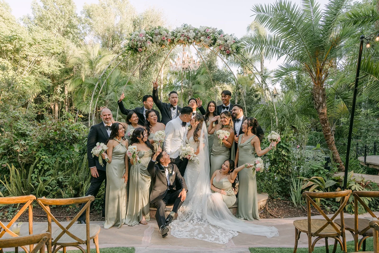 The wedding party cheering around Nicole and Caryl under the ceremony arch at Eden Gardens.