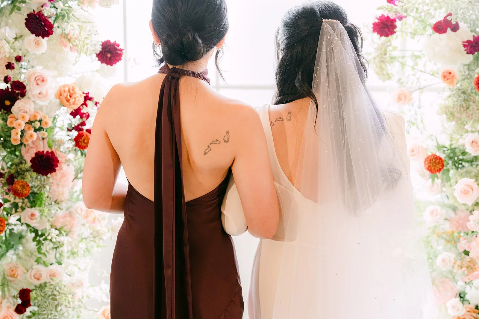 Denise and her sister from behind, burgundy open-back dress and cathedral veil.