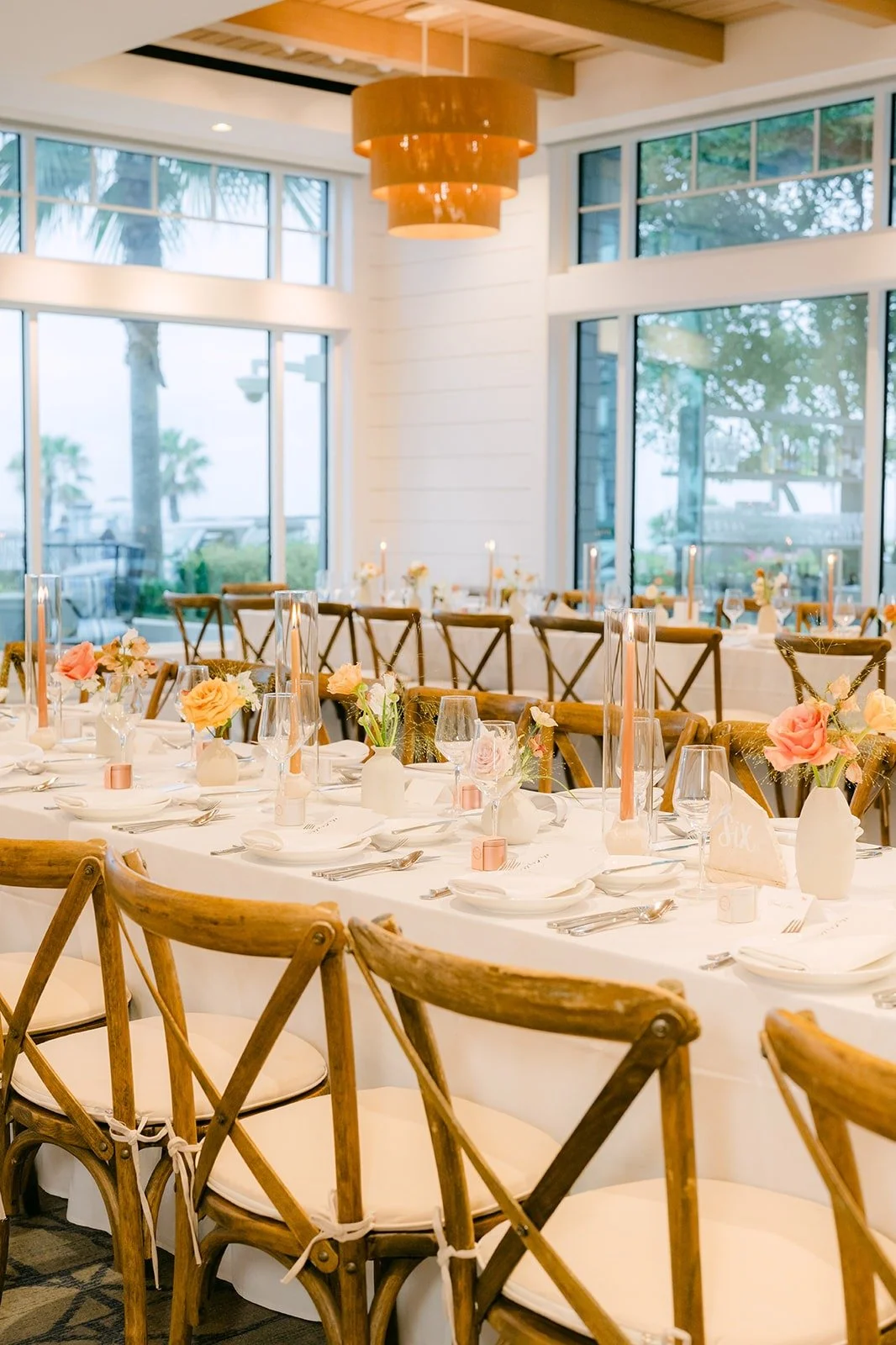 Long tables with cross back chairs beside the ballroom windows
