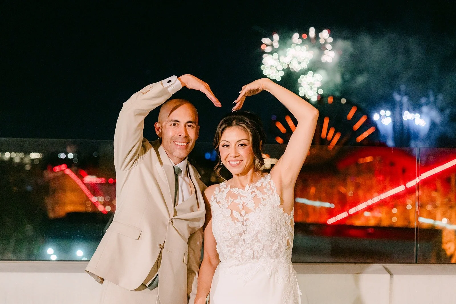 Francesca and Daniel make a heart with their hands under the fireworks on the Jewel Terrace, photographed by One and Only Production