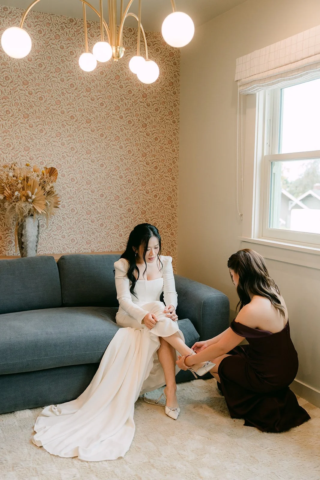 A bridesmaid helps Denise with her shoes in the bridal suite.
