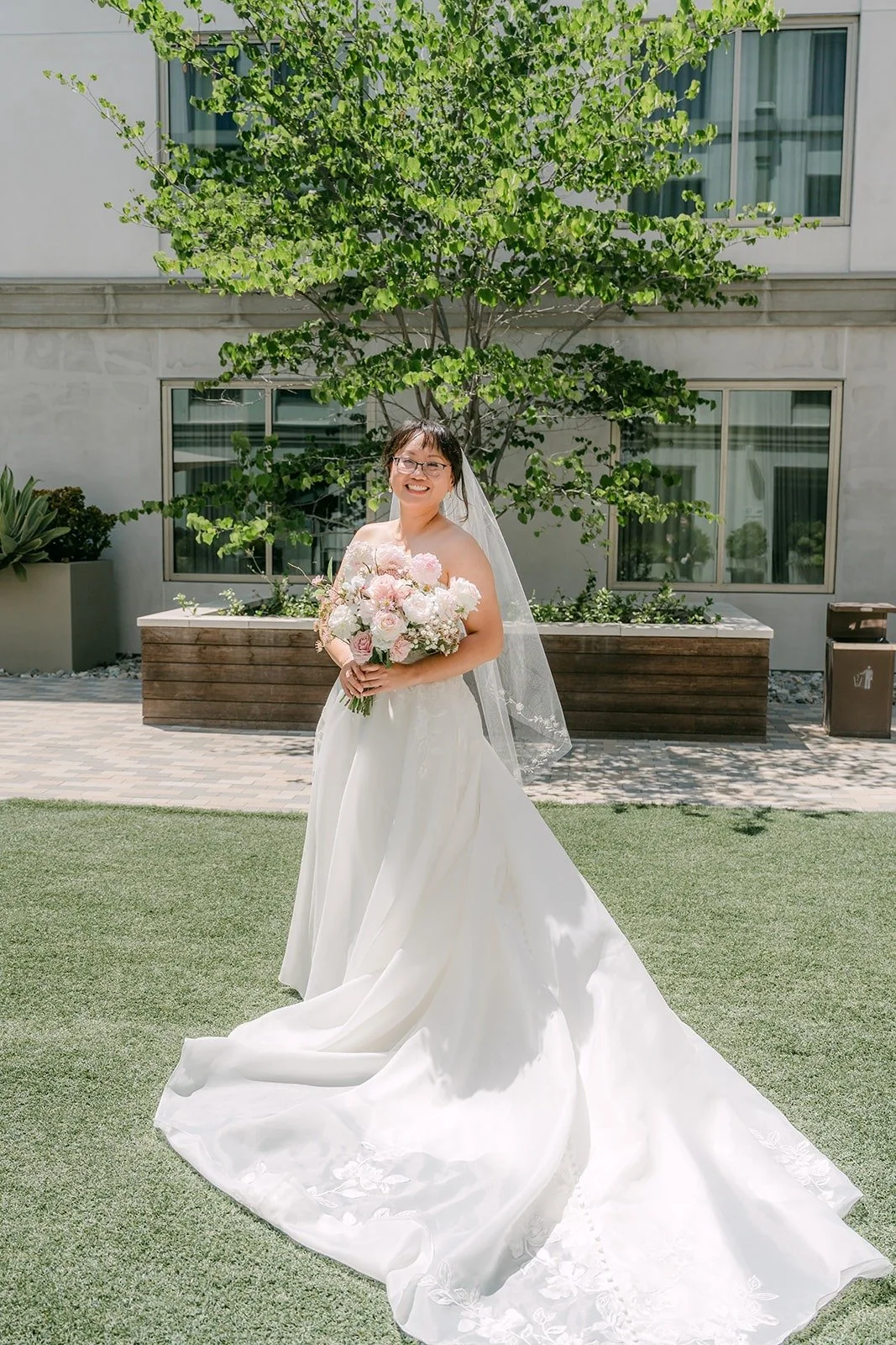 Stella in her strapless ivory gown and long veil standing on the courtyard lawn at the Sheraton