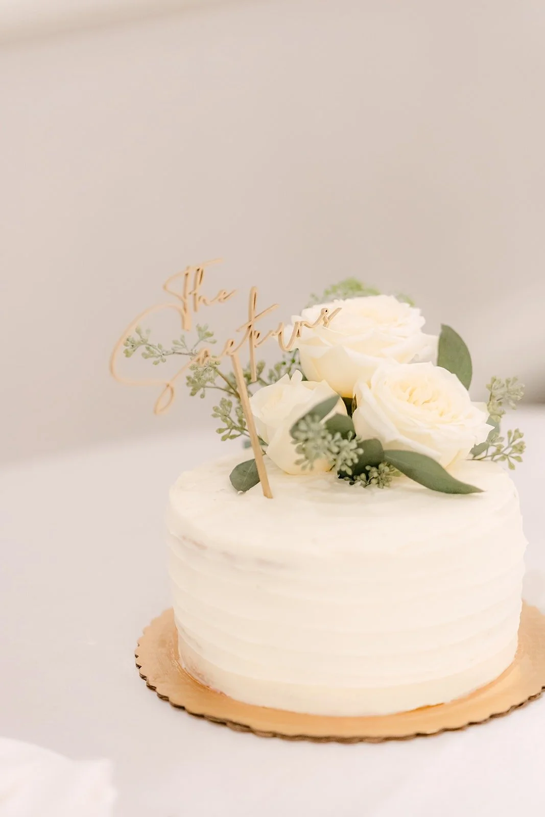 White cake topped with white roses and dried florals