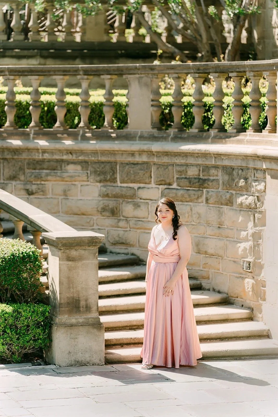 Saira in a blush satin gown at the foot of the stone staircase in Greystone's lower gardens.