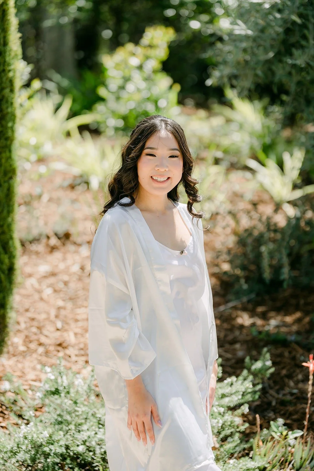 Kelli in a white satin robe standing in the garden at Los Robles Greens
