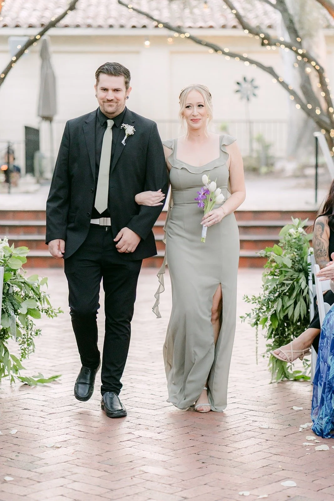 A bridesmaid in sage green walking down the aisle with a friend of the couple