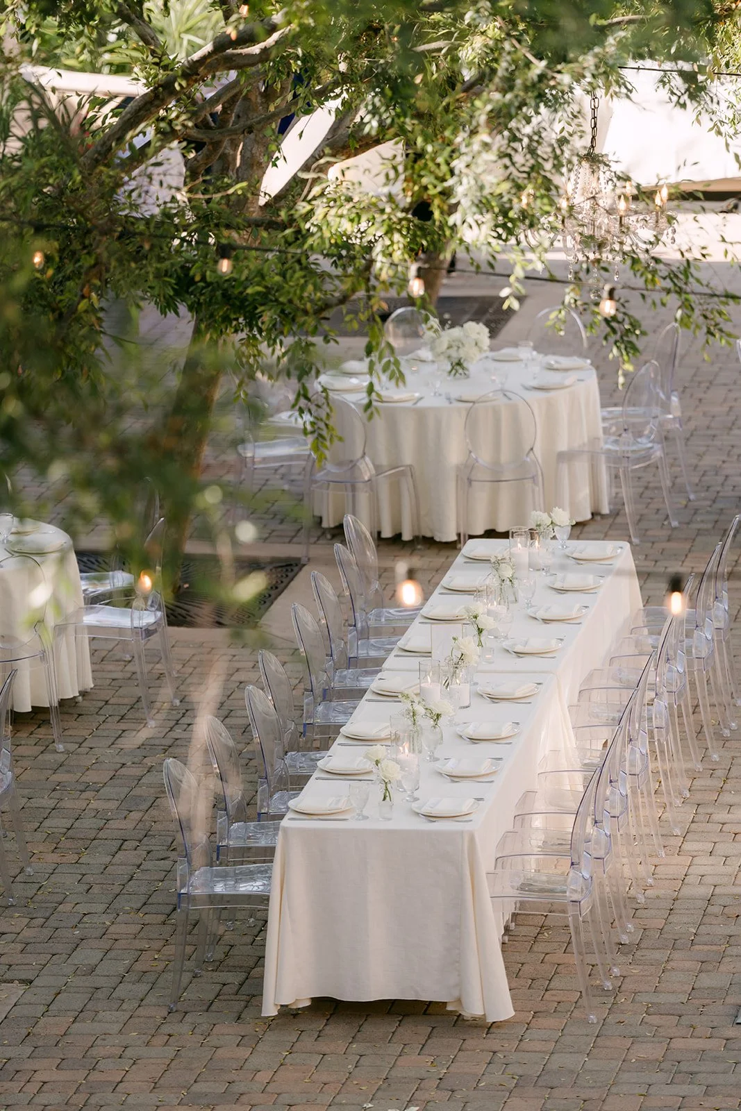 Long reception table with ghost chairs under the trees