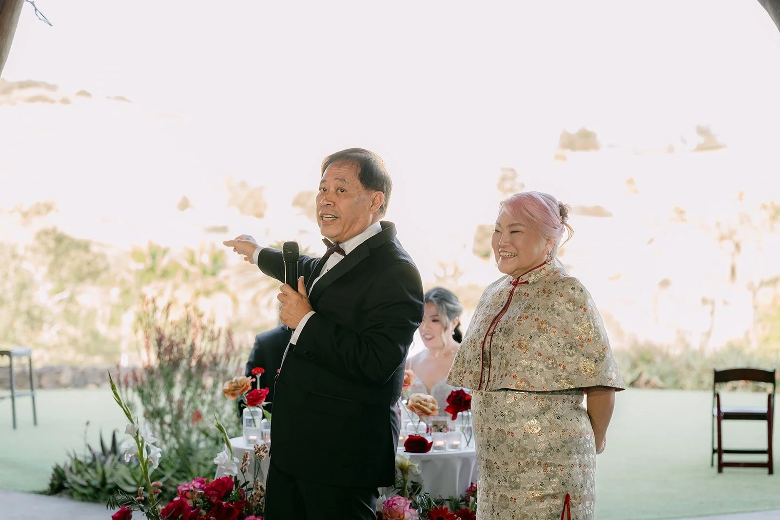 A guest giving a speech beside a family member with the hills behind them