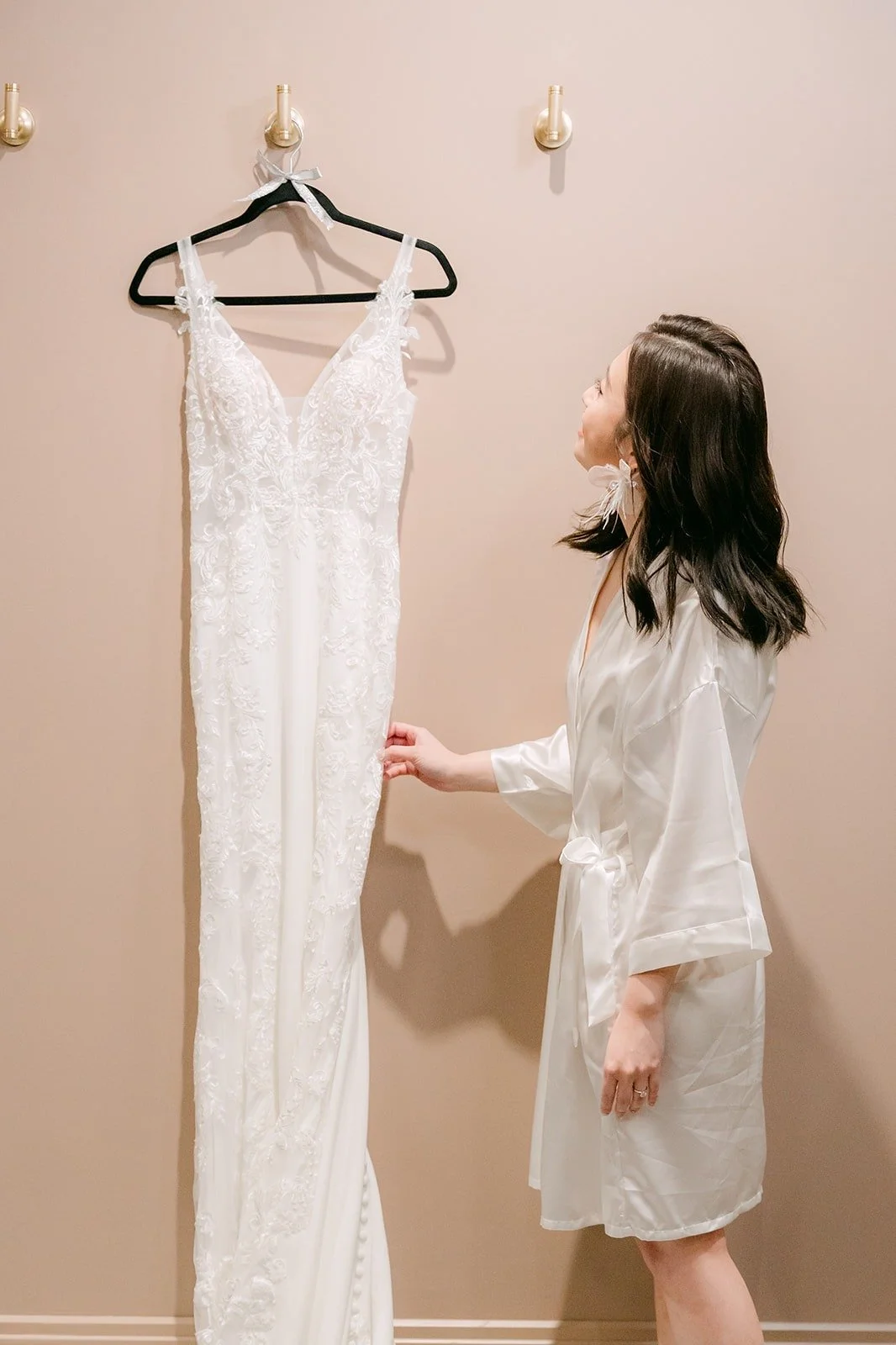 Elisa in a white robe looks at her wedding gown on its hanger
