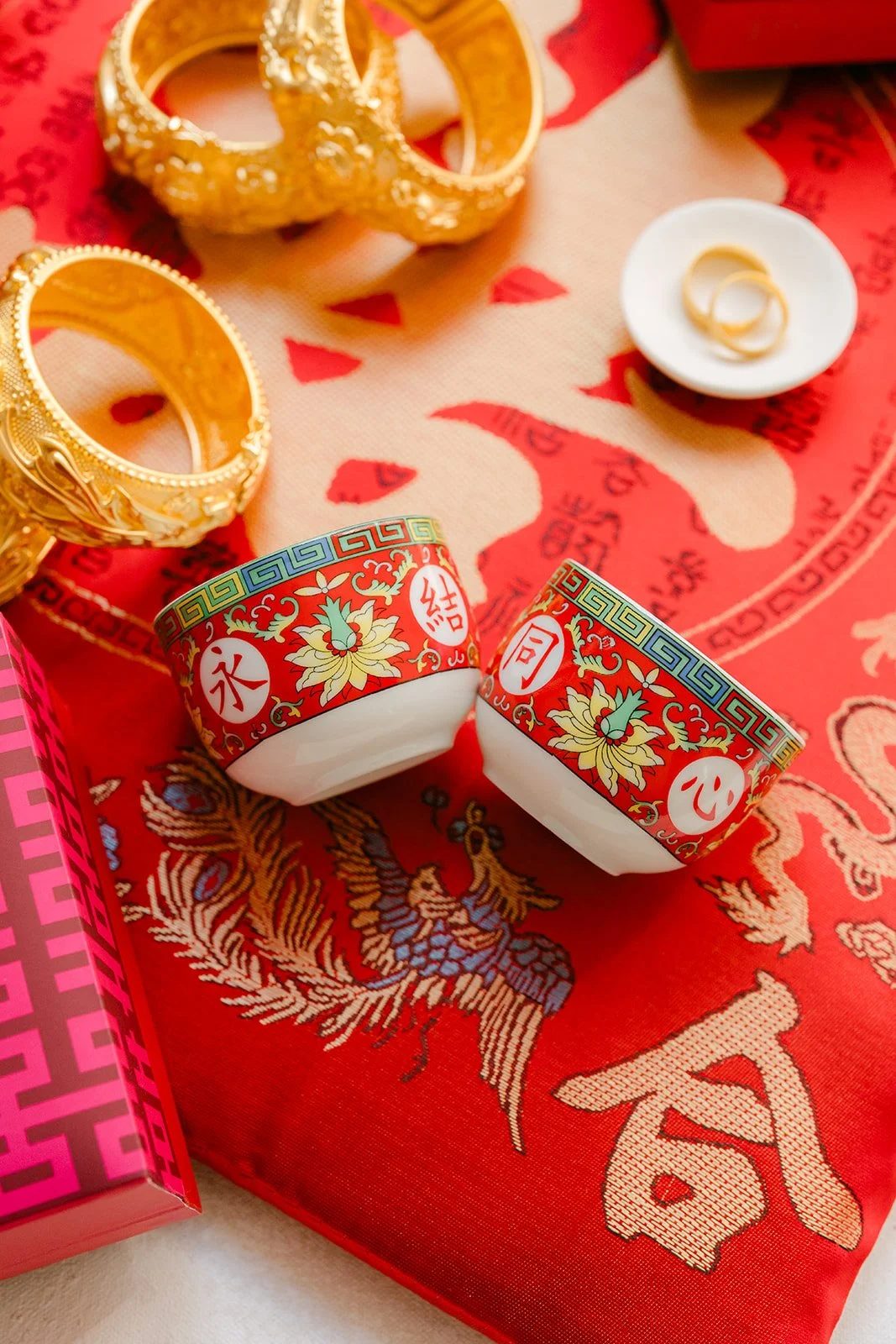 Gold dragon and phoenix bangles beside red double happiness teacups.