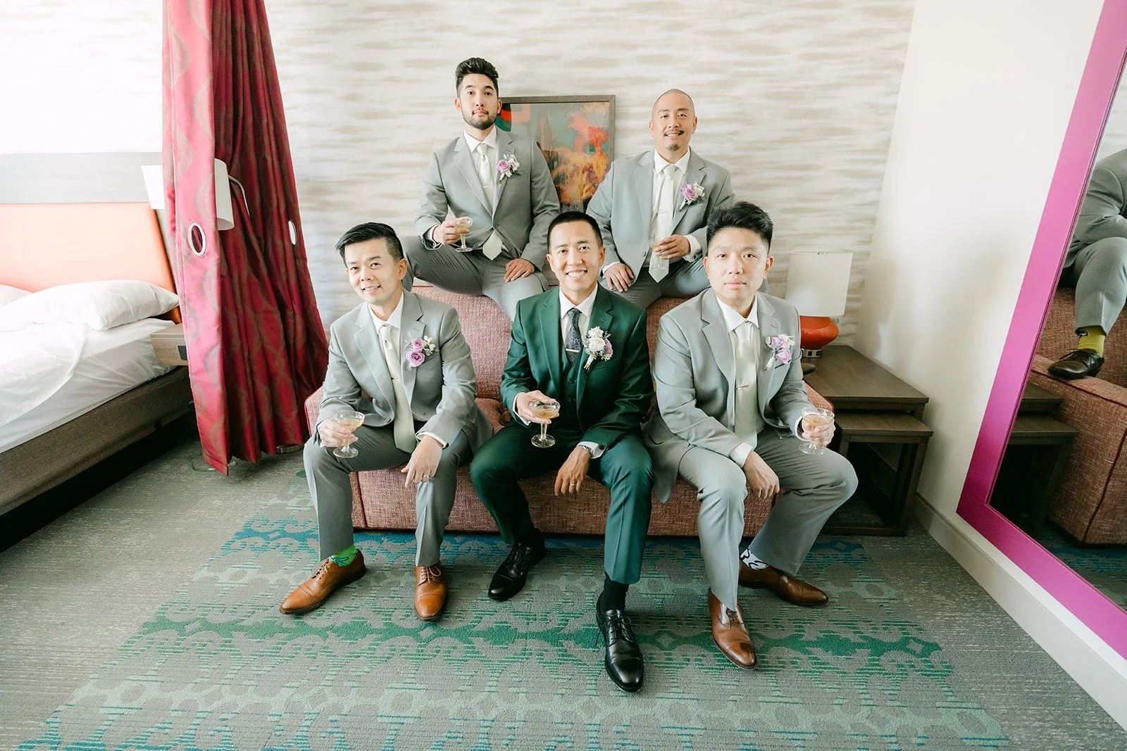 Kevin and his groomsmen in light grey suits relax on the hotel sofa