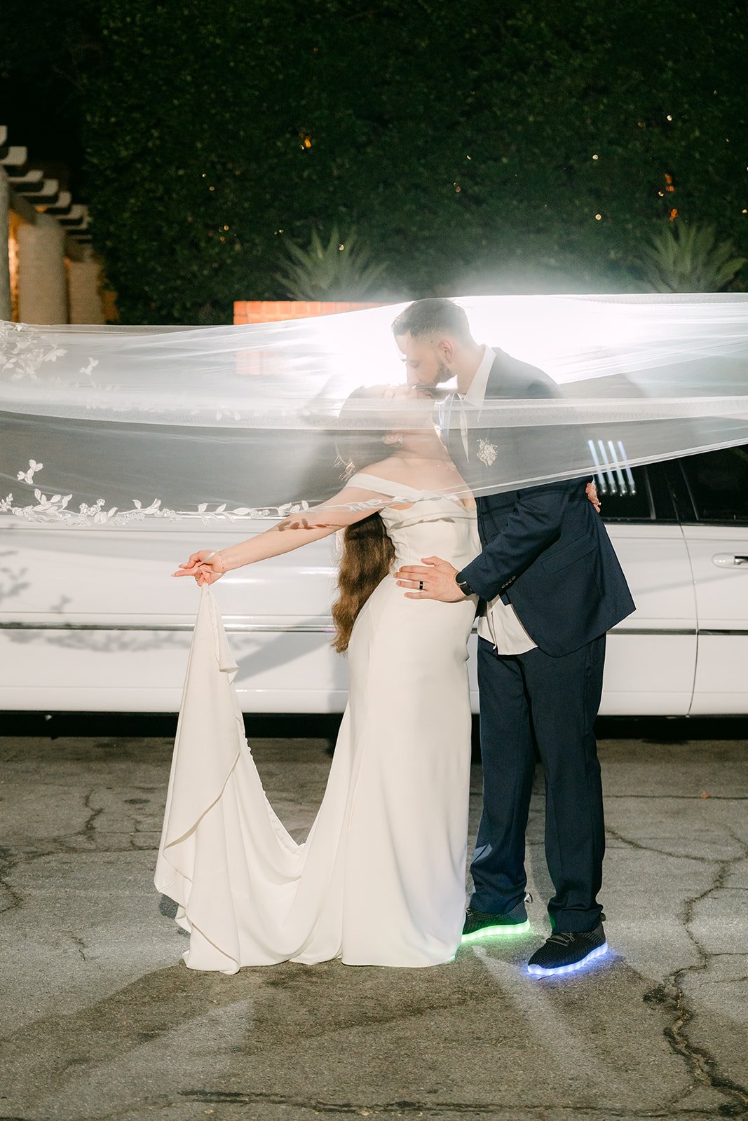 Couple wrapped in her veil in front of the white limo, light up sneakers glowing